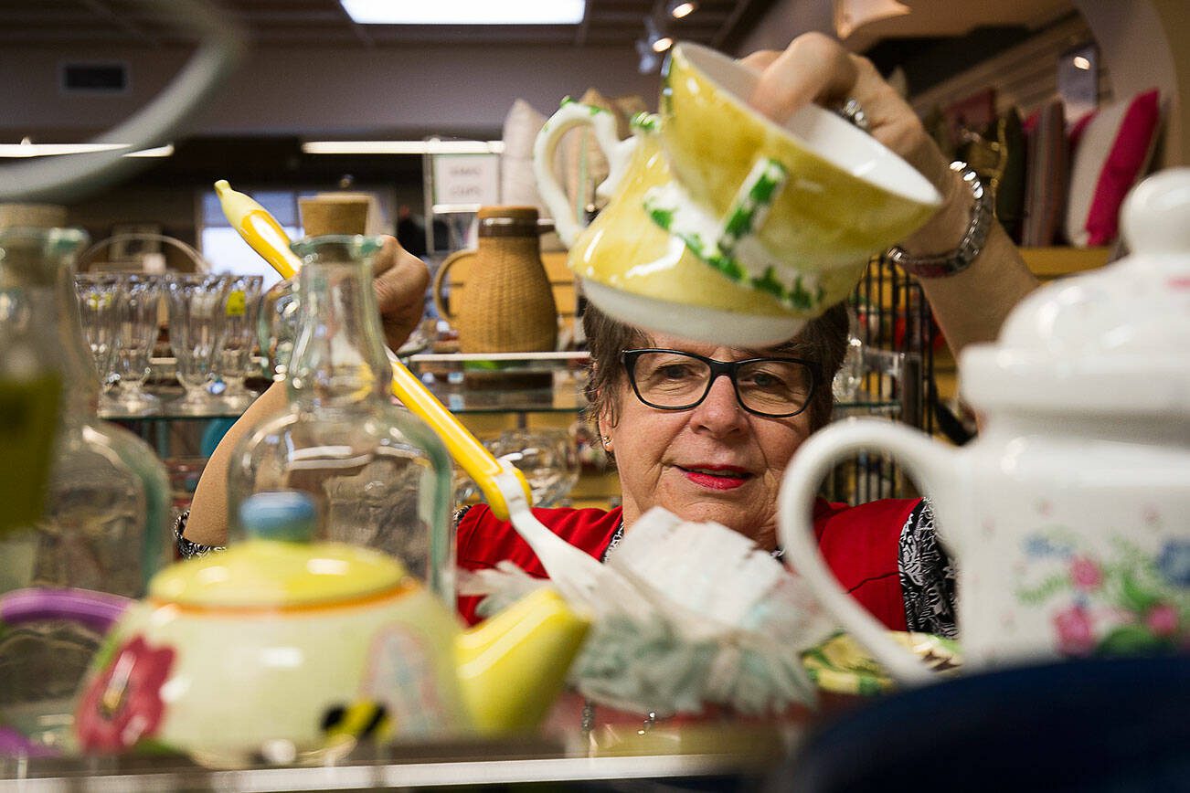 Volunteer Judi Drake dusts under and around teapots at the Assistance League of Everett on Monday, Nov. 18, 2019 in Everett, Wash. They sell items at their thrift store and donate all the proceeds to families in Snohomish County. All of the 300 people who help out are volunteers. (Andy Bronson / The Herald)