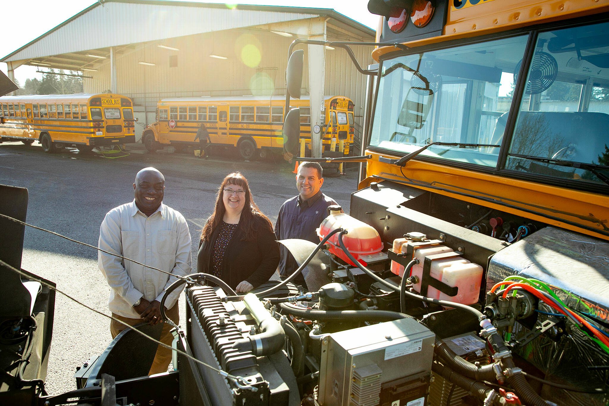 Snohomish School District transportation supervisors John Kwesele, left, and Karl Hereth, right, stand with Transportation Director Veronica Schmidt behind the open hood of the district’s first electric school bus Thursday, March 7, 2024, at the district bus depot in Snohomish, Washington. (Ryan Berry / The Herald)