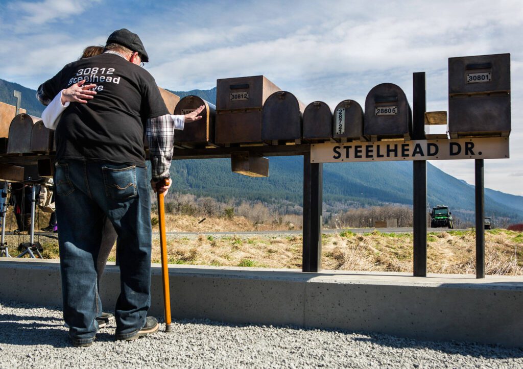 Ron Thompson, right, embraces his wife Gail Thompson, left, as she reaches out to touch a replica of their mailbox during the Oso slide remembrance ceremony on Friday, March 22, 2019 in Oso, Washington. (Olivia Vanni / The Herald)
