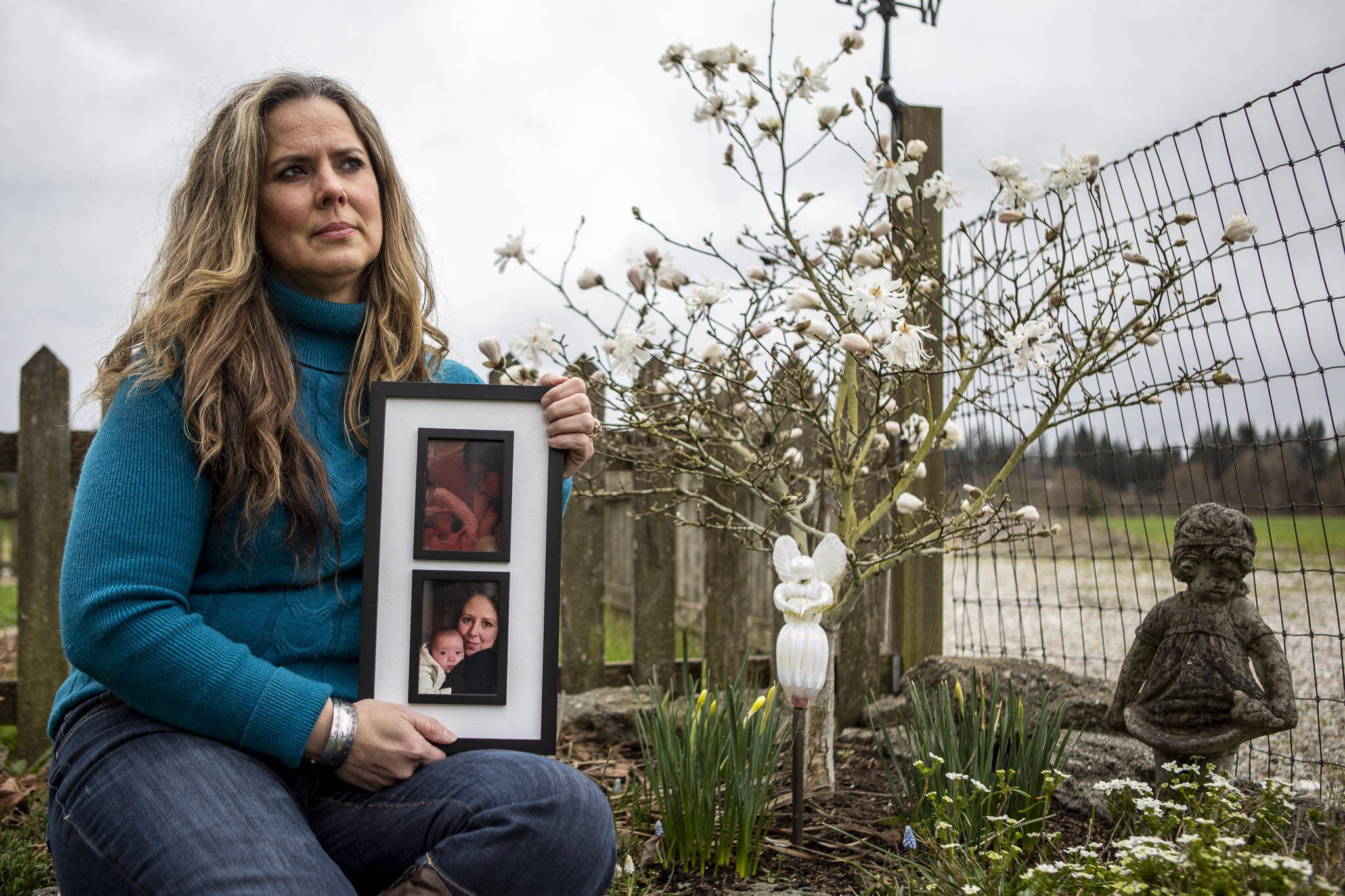 Julie Petersen poses for a photo with images of her sister Christina Jefferds and Jefferds’ grand daughter Sanoah Violet Huestis next to a memorial for Sanoah at her home on March 20, 2024 in Arlington, Washington. Peterson wears her sister’s favorite color and one of her bangles. (Annie Barker / The Herald)
