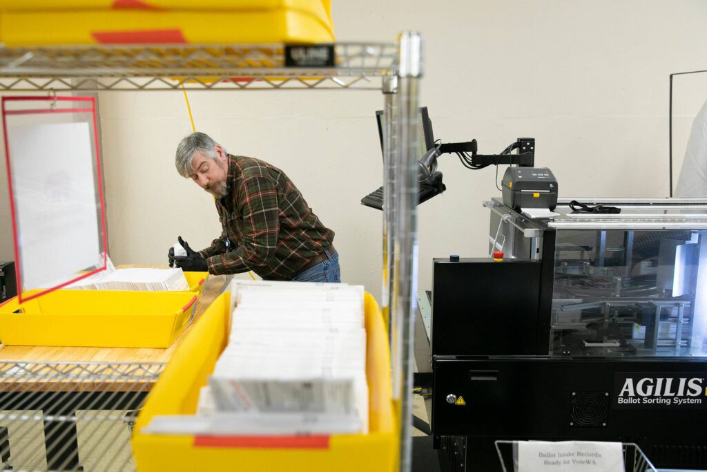 An election worker feeds ballots into a sorting machine. (Ryan Berry / The Herald)
