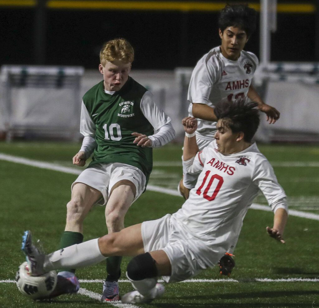 Archbishop Murphy’s Gabe Herrera (10) slides to knock the ball away from Edmonds-Woodway’s Ben Hanson during a match on March 28, 2023, in Edmonds. (Annie Barker / The Herald)
