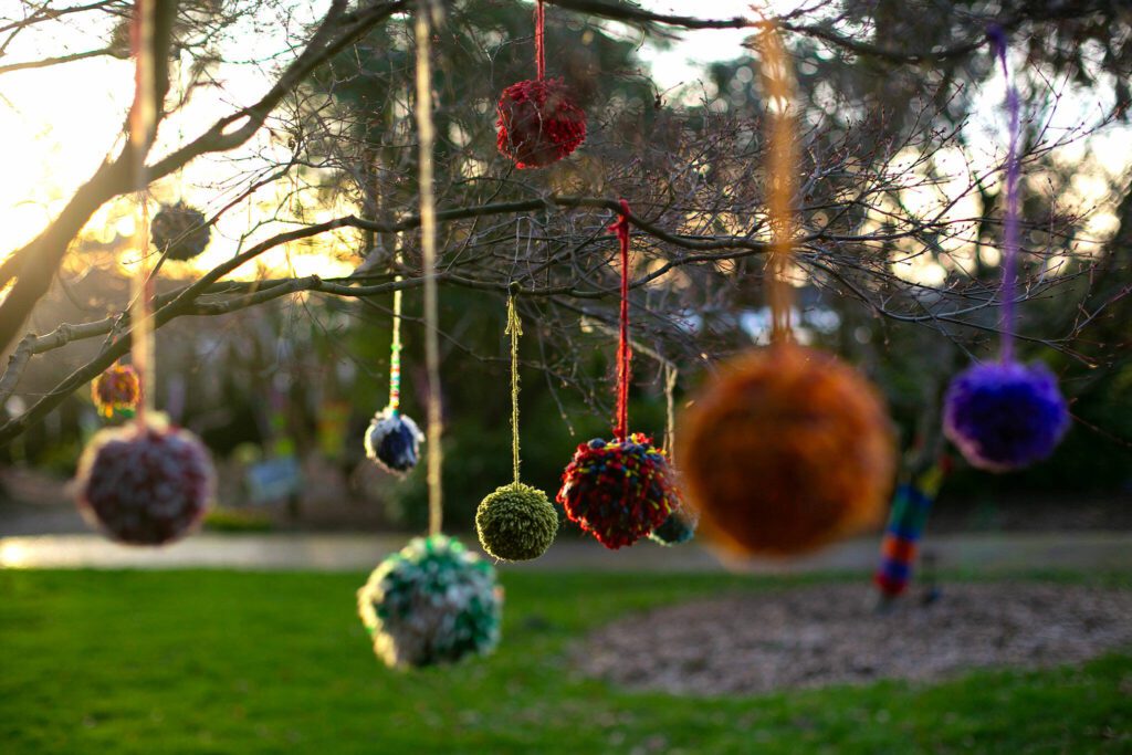 Dozens of yarn pompoms hang from a number of trees as part of Color Storm at Evergreen Arboretum and Gardens on Thursday, March 14, 2024, in Everett, Washington. (Ryan Berry / The Herald)
