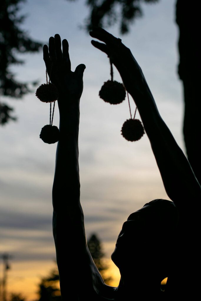 Yarn pompoms hang from the fingers of a statue as part of Color Storm event at Evergreen Arboretum and Gardens on Thursday, March 14, 2024, in Everett, Washington. (Ryan Berry / The Herald)
