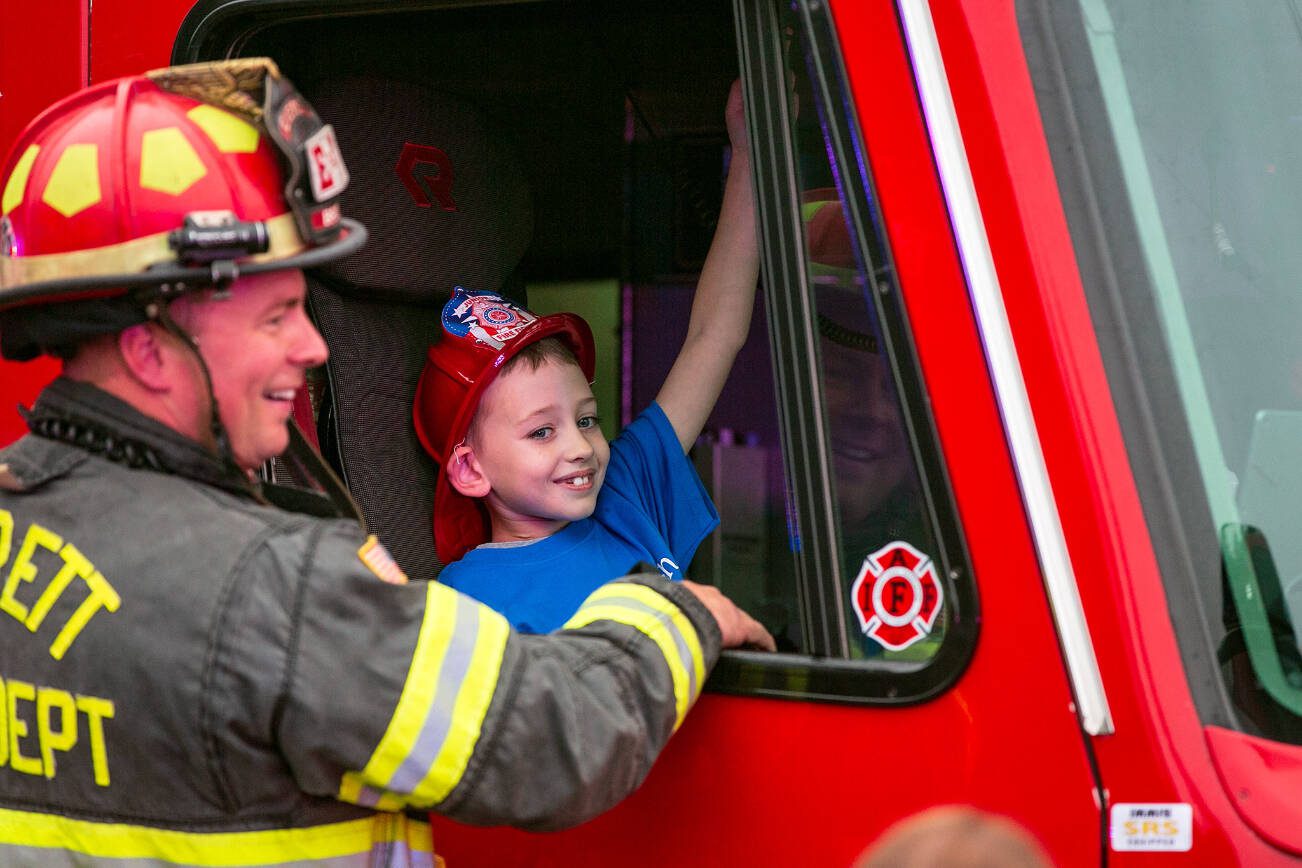 Carson gets a chance to sound the horn in an Everett Fire Department engine with the help of captain Jason Brock during a surprise Make-A-Wish sendoff Saturday, Oct. 21, 2023, at Thornton A. Sullivan Park in Everett, Washington. (Ryan Berry / The Herald)