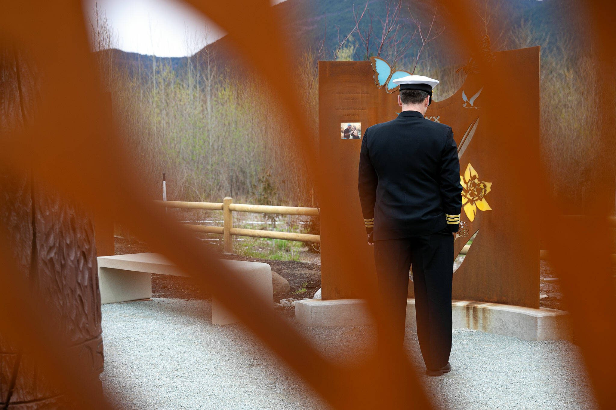 A firefighter stands in silence before a panel bearing the names of L. John Regelbrugge and Kris Regelbrugge during the ten-year remembrance of the Oso landslide on Friday, March 22, 2024, at the Oso Landslide Memorial in Oso, Washington. (Ryan Berry / The Herald)