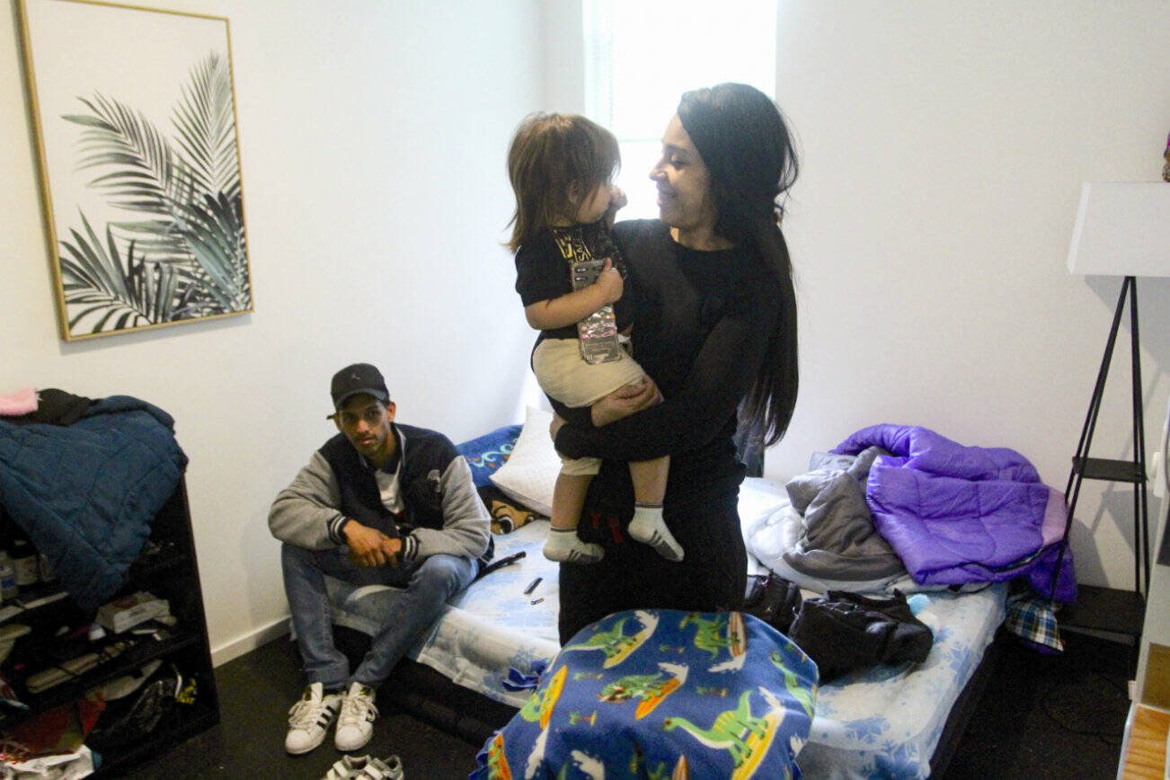 Barbara Peraza-Garcia holds her 2-year-old daughter, Frailys, while her partner Franklin Peraza sits on their bed in their 'micro apartment' in Seattle on Monday, March 11, 2024. (AP Photo/Manuel Valdes)