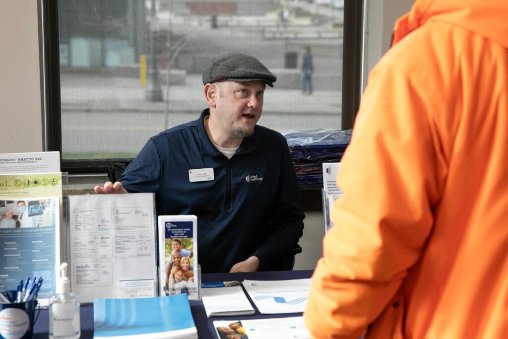 Jason Hauff, community engagement manager with United Healthcare, speaks with people about Medicaid options during a resource fair at the Carnegie Resource Center on Wednesday, March 6, 2024, in downtown Everett, Washington. (Ryan Berry / The Herald)
