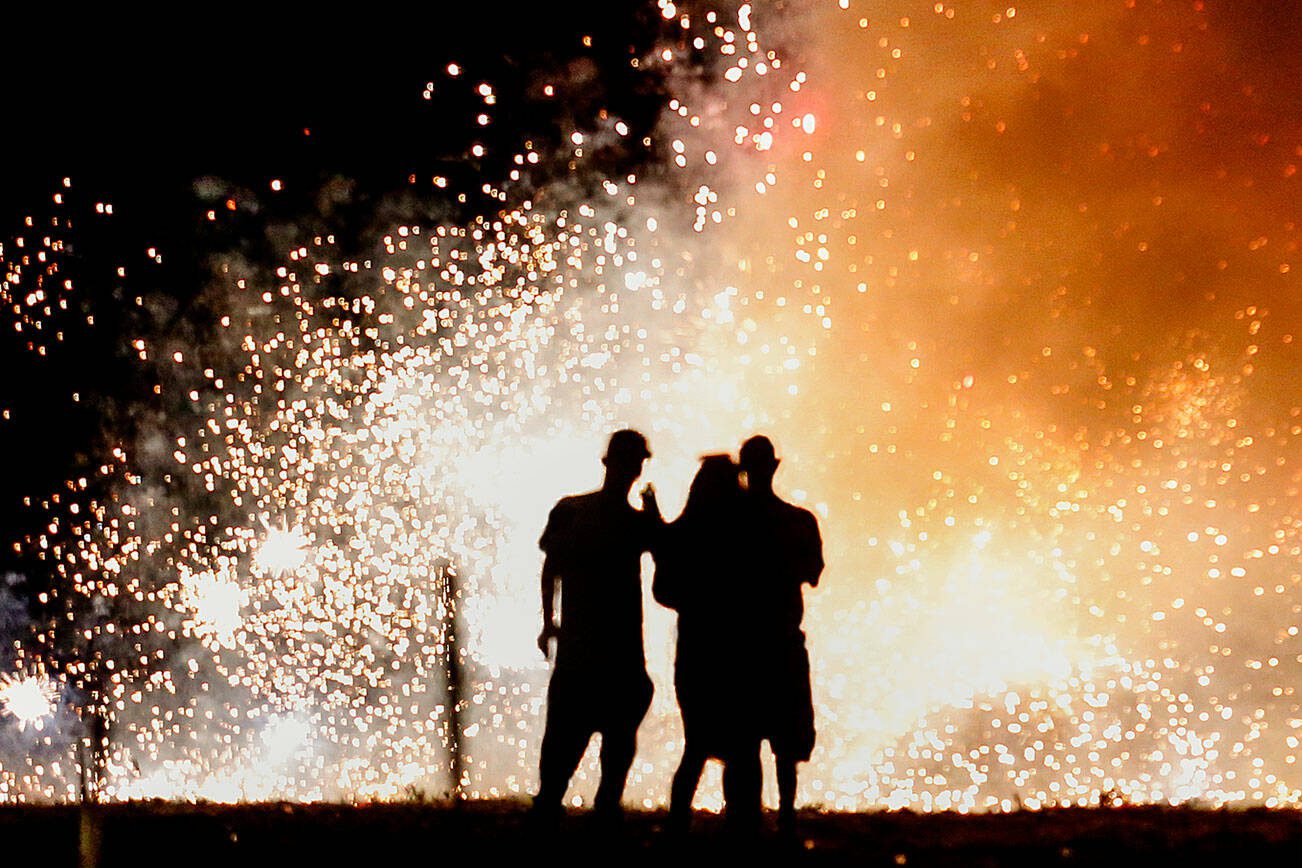 A trio in the lighting area at Boom City watches a shower of white-hot sparks from several fountains set off Tuesday just as darkness falls.  (Dan Bates / The Herald)