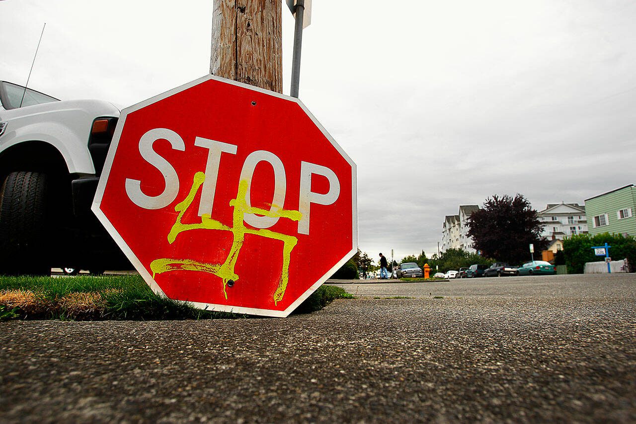 A stop sign defaced with a spray-painted swastika sits on the ground at the corner of 25th Street and Rucker Avenue while a City of Everett worker installs a new sign in the summer of 2009. (Dan Bates / Herald file photo)