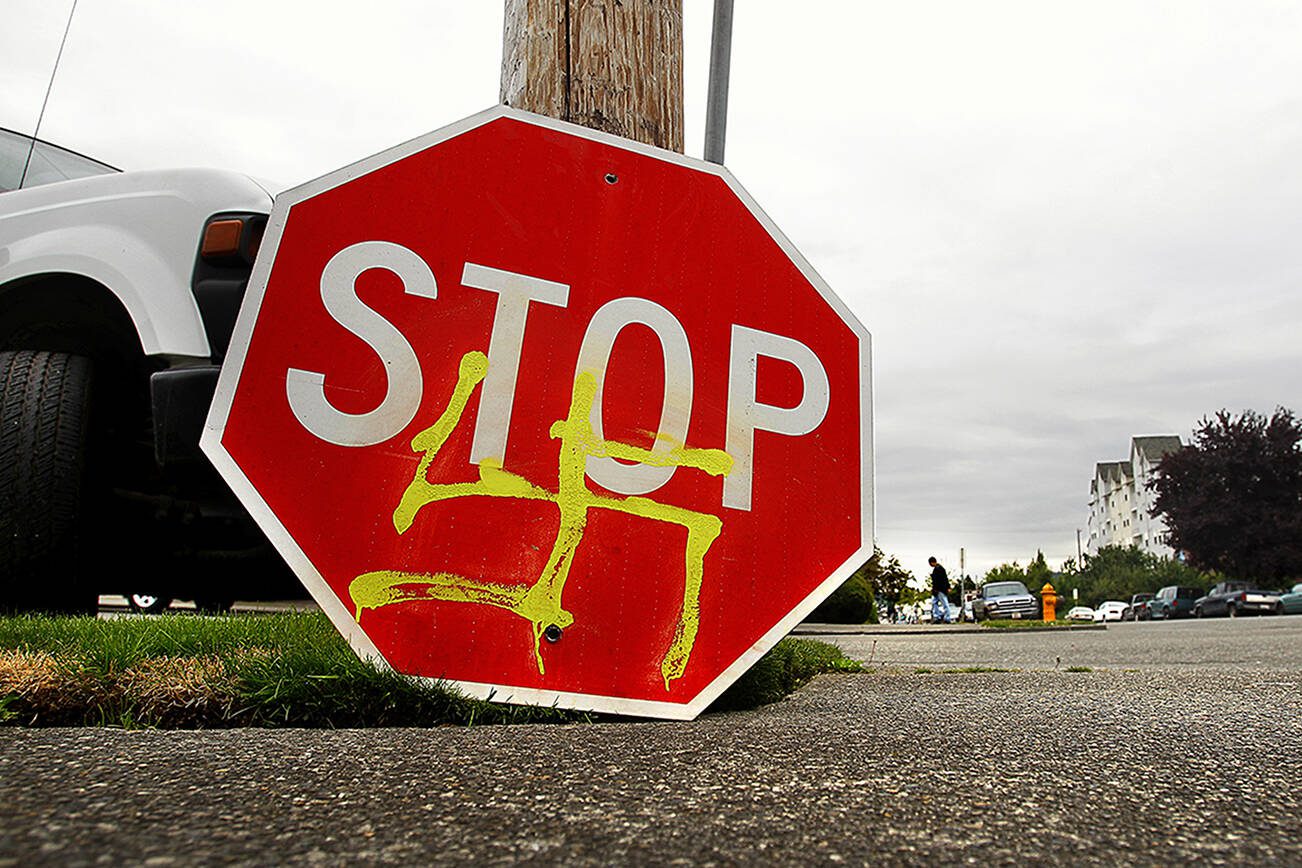A stop sign defaced with a spray-painted swastika is on the ground at the corner of 25th street and Rucker Avenue while a City of Everett worker installs a new one in the summer of 2009.  (Dan Bates / The Herald) 






Bates / The Herald)