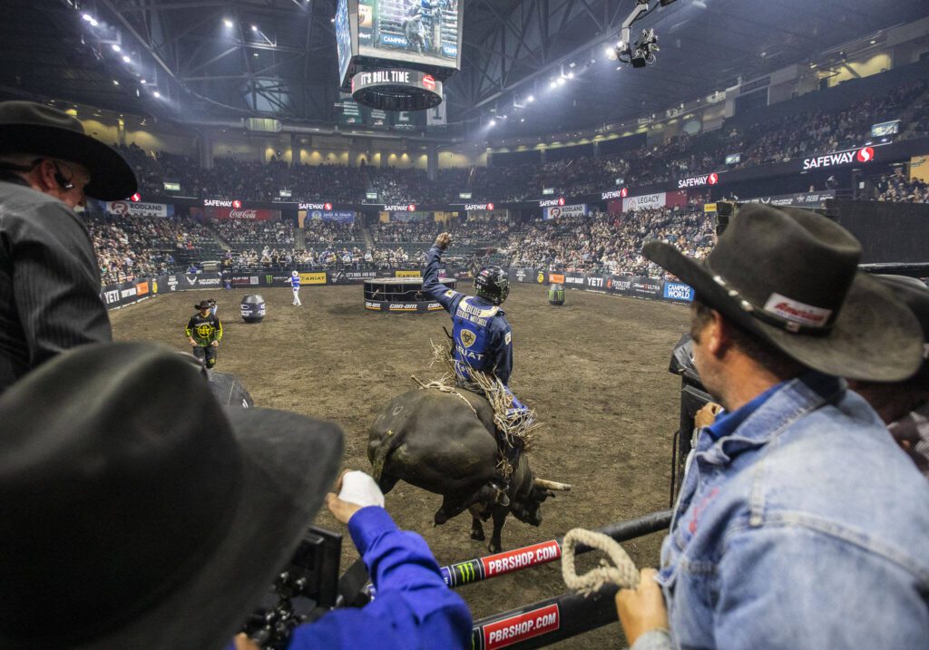 Ezekiel Mitchell raises his arm as the bull Electric Kitty jumps out of the chute during PBR Everett at Angel of the Winds Arena on Wednesday, April 17, 2024 in Everett, Washington. (Olivia Vanni / The Herald)
