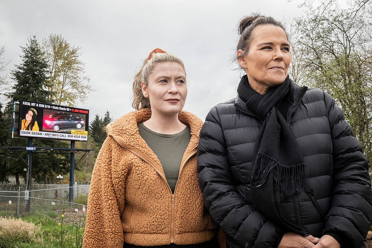 Carol McKinnon, right, the mother of Taylor Druliner, and Druliner’s best friend Brecca Blas, left, stand in front of a billboard searching for the suspect in the fatal hit and run of Taylor Druliner on Tuesday, April 9, 2024 in Everett, Washington. (Olivia Vanni / The Herald)