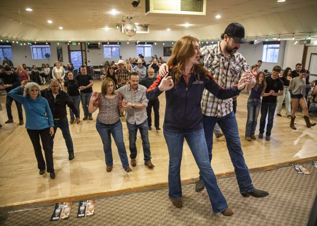 Country dance instructor Jen Workman, left, and husband Brian Workman, right, go through steps on stage with a country dance class at Normanna Lodge on Tuesday, April 9, 2024 in Everett, Washington. (Olivia Vanni / The Herald)
