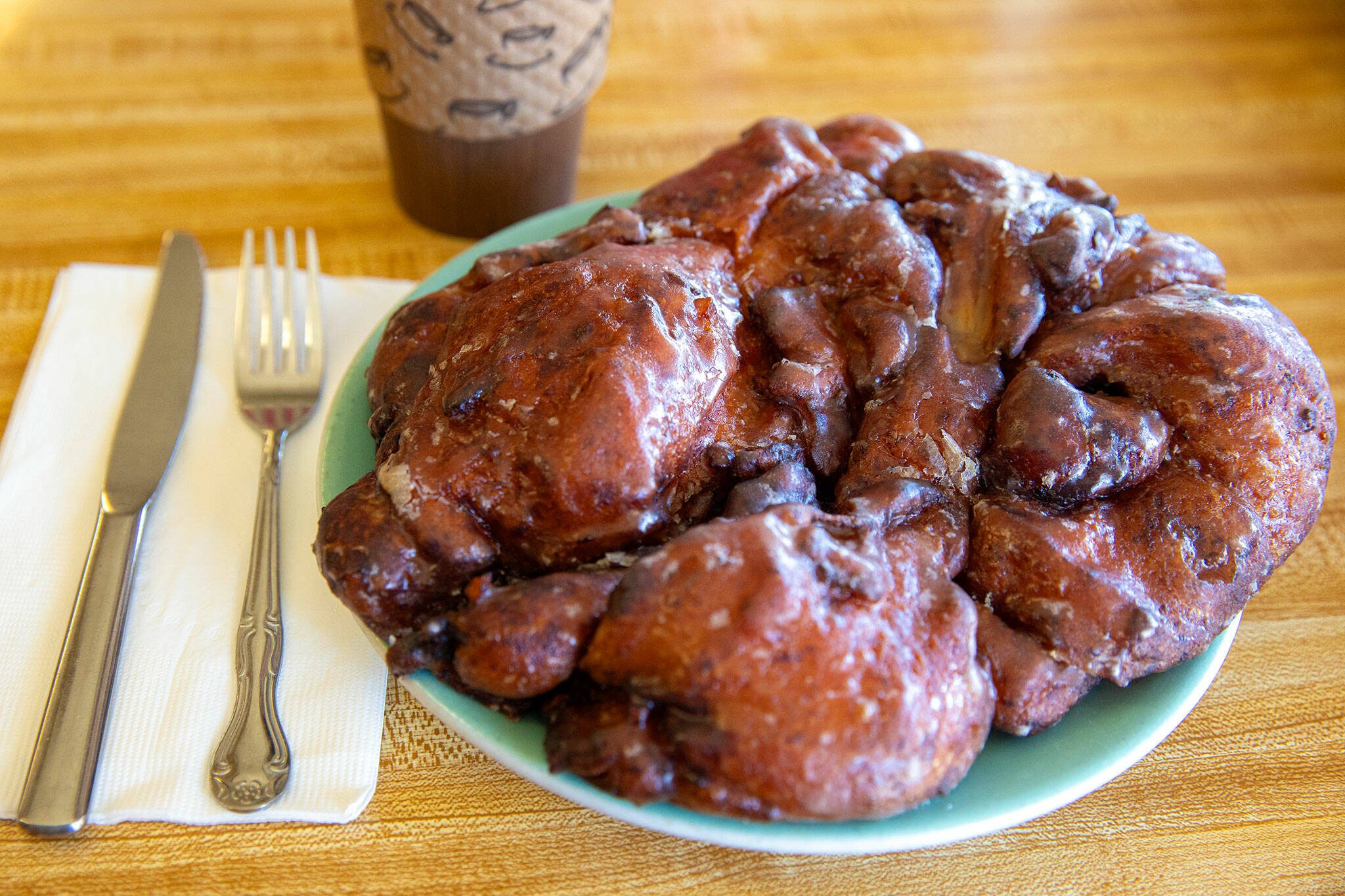 A giant $7 apple fritter eclipses a plate on Wednesday, April 17, 2024, at Karl’s Bakery in Everett, Washington. (Ryan Berry / The Herald)