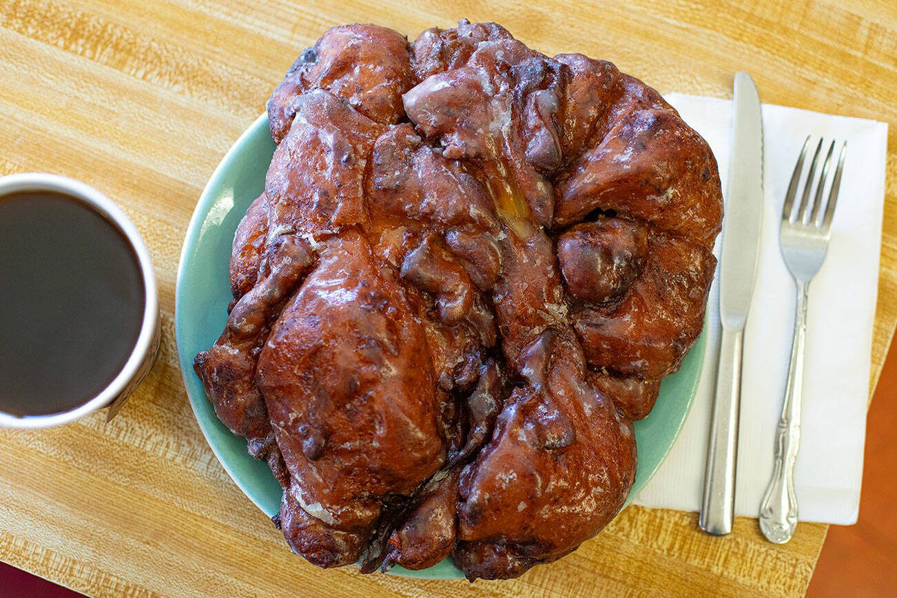 A giant seven-dollar apple fritter eclipses a plate on Wednesday, April 17, 2024, at Karl’s Bakery in Everett, Washington. (Ryan Berry / The Herald)