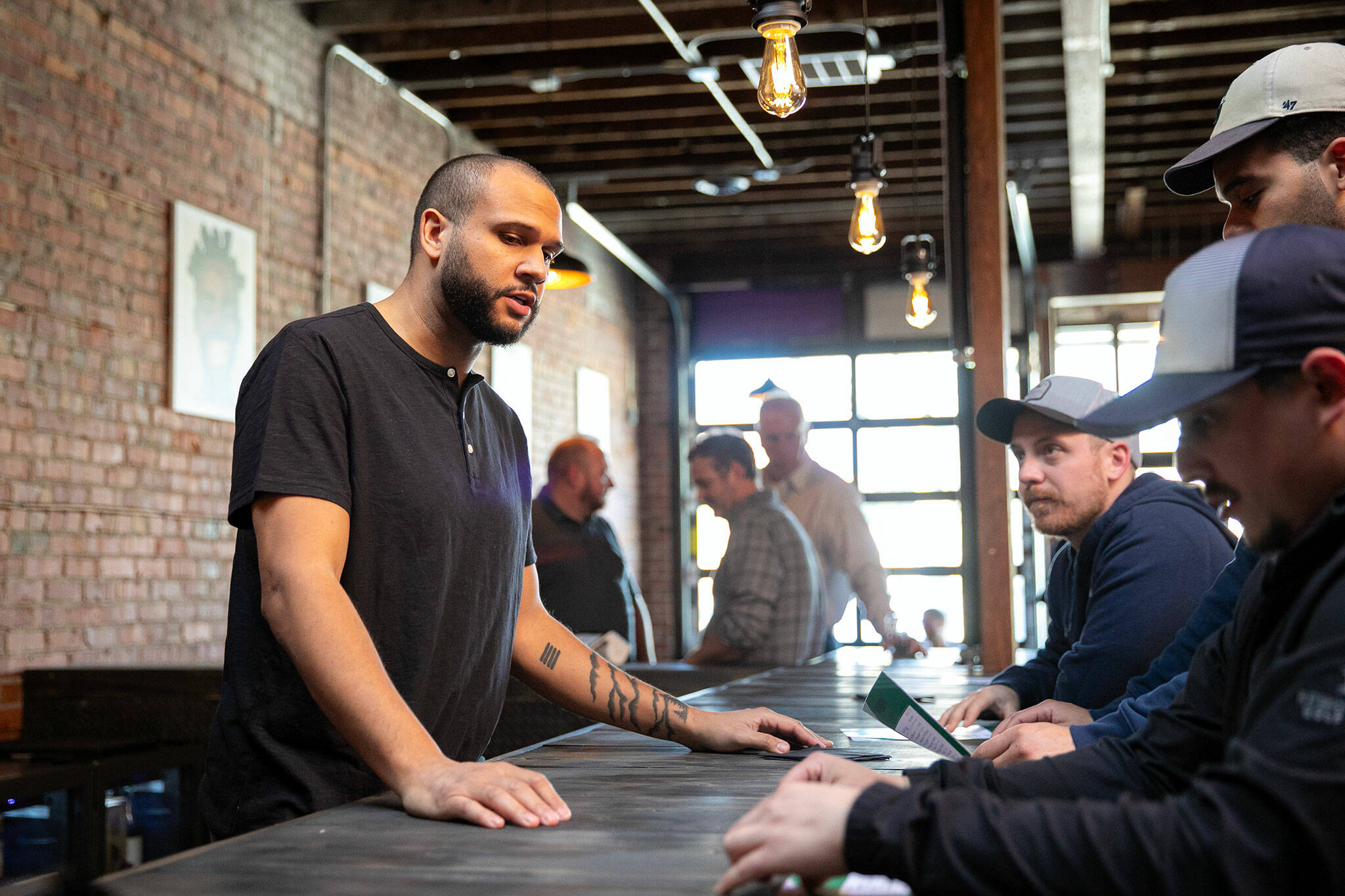 Craig Chambers chats with a couple of guests while tending the bar at Obsidian Beer Hall on Friday, April 12, 2024, in downtown Everett, Washington. (Ryan Berry / The Herald)