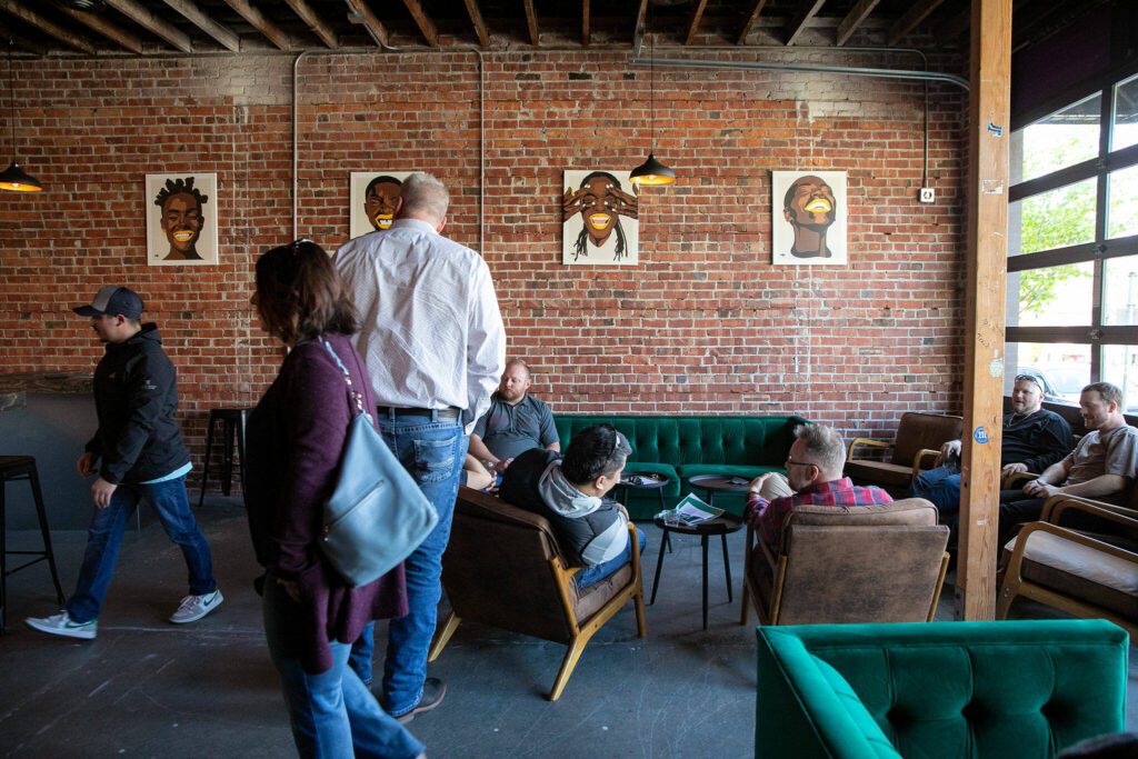 People make themselves at home at the front of Obsidian Beer Hall on Friday, April 12, 2024, in downtown Everett, Washington. Art by Jessie Lipscomb or Momma Lips Draws hangs on the wall behind them.
