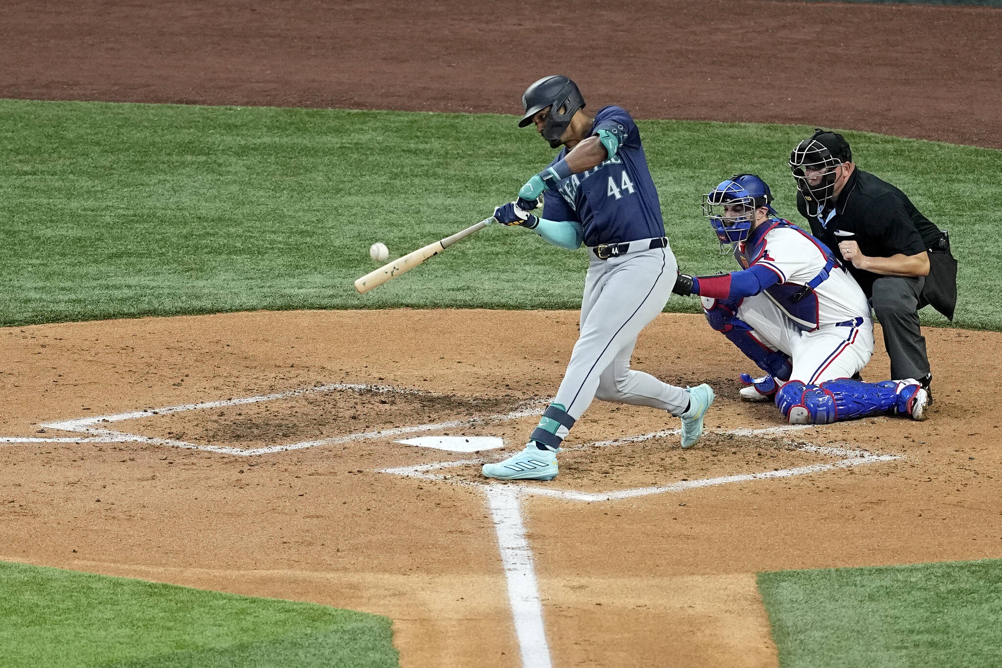 Seattle Mariners star Julio Rodriguez connects for a two-run home run next to Texas Rangers catcher Jonah Heim and umpire Mark Carlson during the third inning of a baseball game in Arlington, Texas, Tuesday, April 23, 2024. It was Rodriguez’s first homer of the season. (AP Photo/Tony Gutierrez)