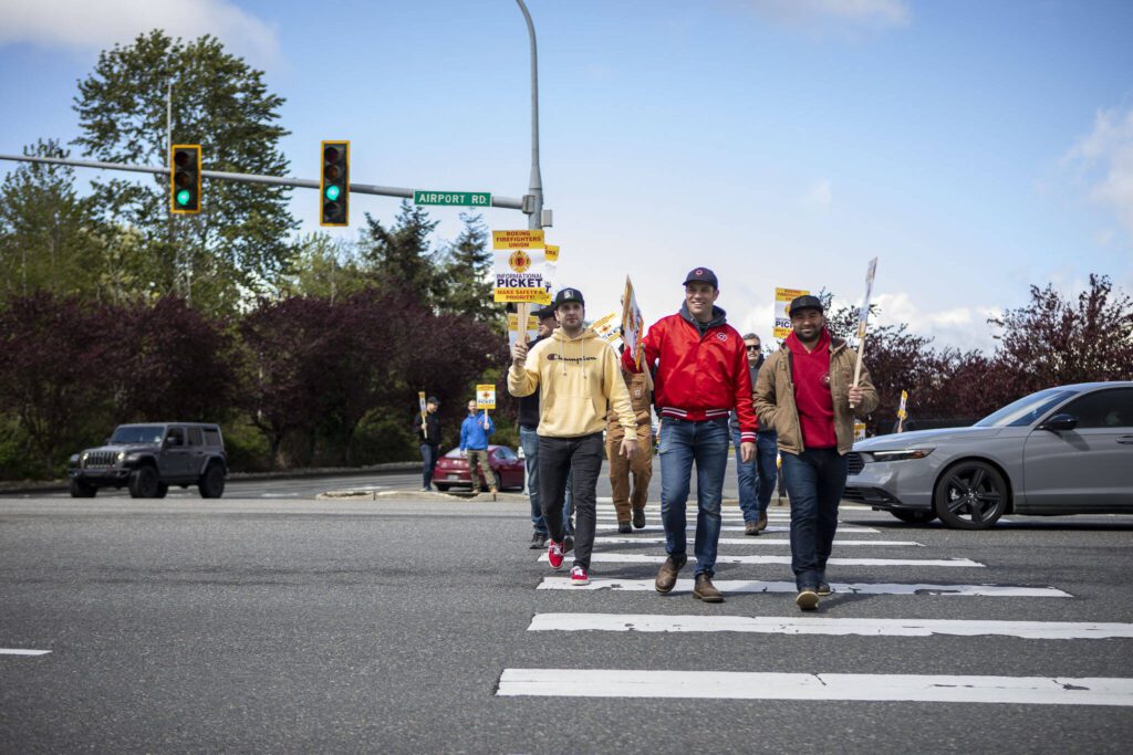 Members of Boeing’s firefighter union and supporters cross the street while holding an informational picket at Airport Road and Kasch Park Road on Monday, April 29, 2024 in Everett, Washington. (Annie Barker / The Herald)

