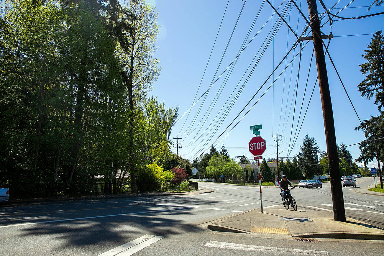 A cyclist crosses the road near the proposed site of a new park, left, at the intersection of Holly Drive and 100th Street SW on Thursday, May 2, 2024, in Everett, Washington. (Ryan Berry / The Herald)