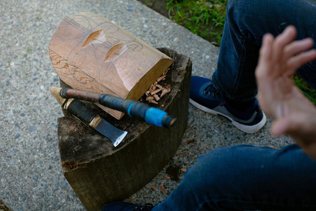 Tlingit Artist Fred Fulmer works on a wooden mask with an adze to demonstrate his carving technique on Wednesday, May 8, 2024, at his home in Everett, Washington. (Ryan Berry / The Herald)

