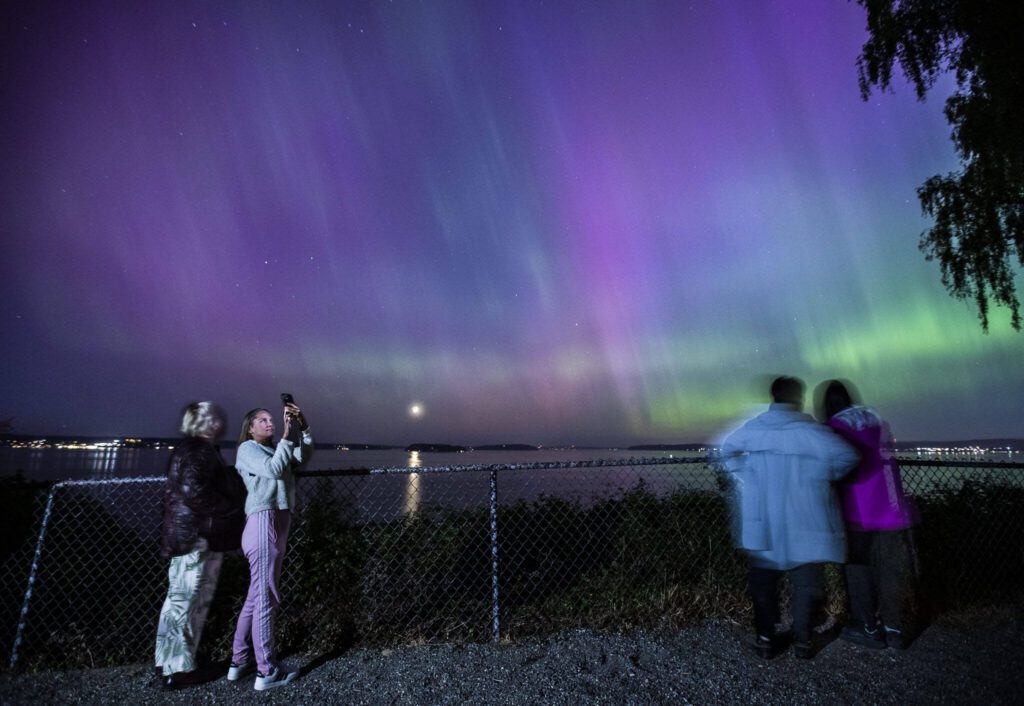 People take photos and videos of the aurora borealis from the outlook at Howarth Park on Friday, May 10, 2024 in Everett, Washington. (Olivia Vanni / The Herald)
