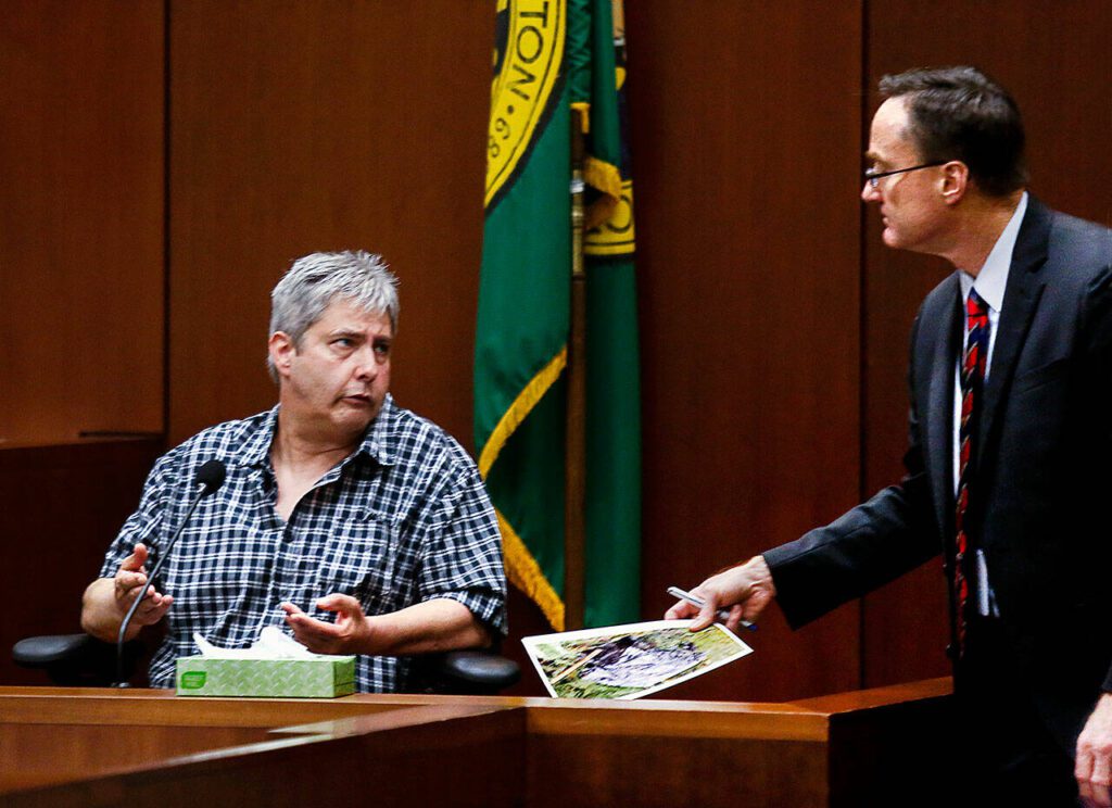 After showing Tony Reed an evidence photo, Snohomish County deputy prosecutor Craig Matheson listens as Reed tries to explain his and his brother John’s attempts to deal with the bodies and everything else. (Dan Bates / The Herald)
