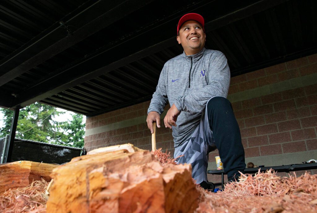 James Madison, a Tulalip and Tlingit tribal member and master woodcarver, stands over a large redwood healing pole that he has been working on for over a month with members of the Archbishop Murphy community on Tuesday, June 13, 2023, in Everett, Washington. When completed, the old-growth artwork will be placed somewhere on campus as a testament to the school’s perseverance through the COVID-19 pandemic. (Ryan Berry / The Herald)
