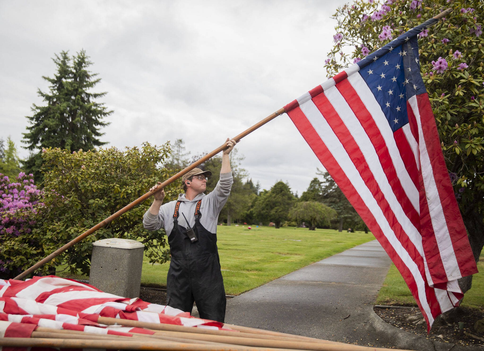 John Pederson lifts a flag in the air while himself and other maintenance crew set up flags for Memorial Day at Floral Hills Cemetery on Friday, May 24, 2024 in Lynnwood, Washington. (Olivia Vanni / The Herald)