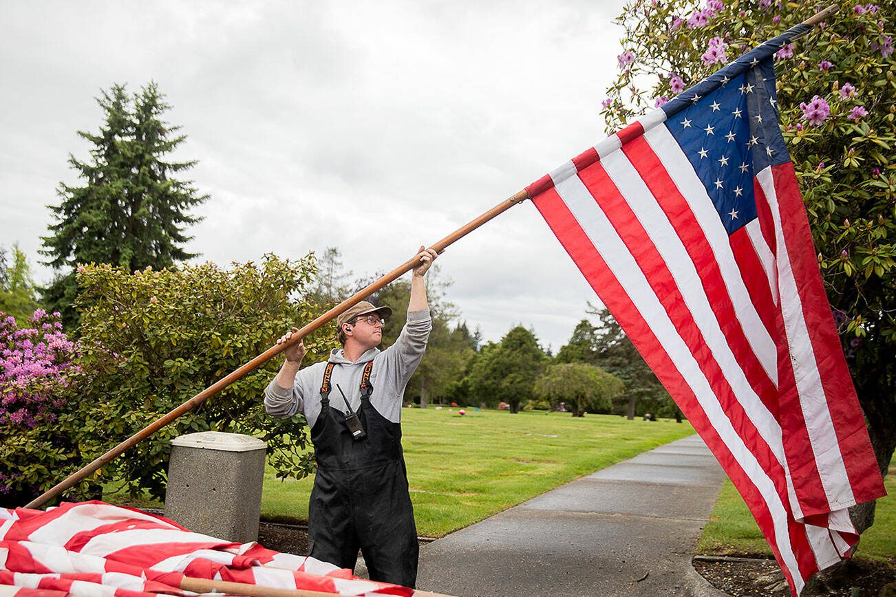 John Pederson lifts a flag in the air while himself and other maintenance crew set up flags for Memorial Day at Floral Hills Cemetery on Friday, May 24, 2024 in Lynnwood, Washington. (Olivia Vanni / The Herald)