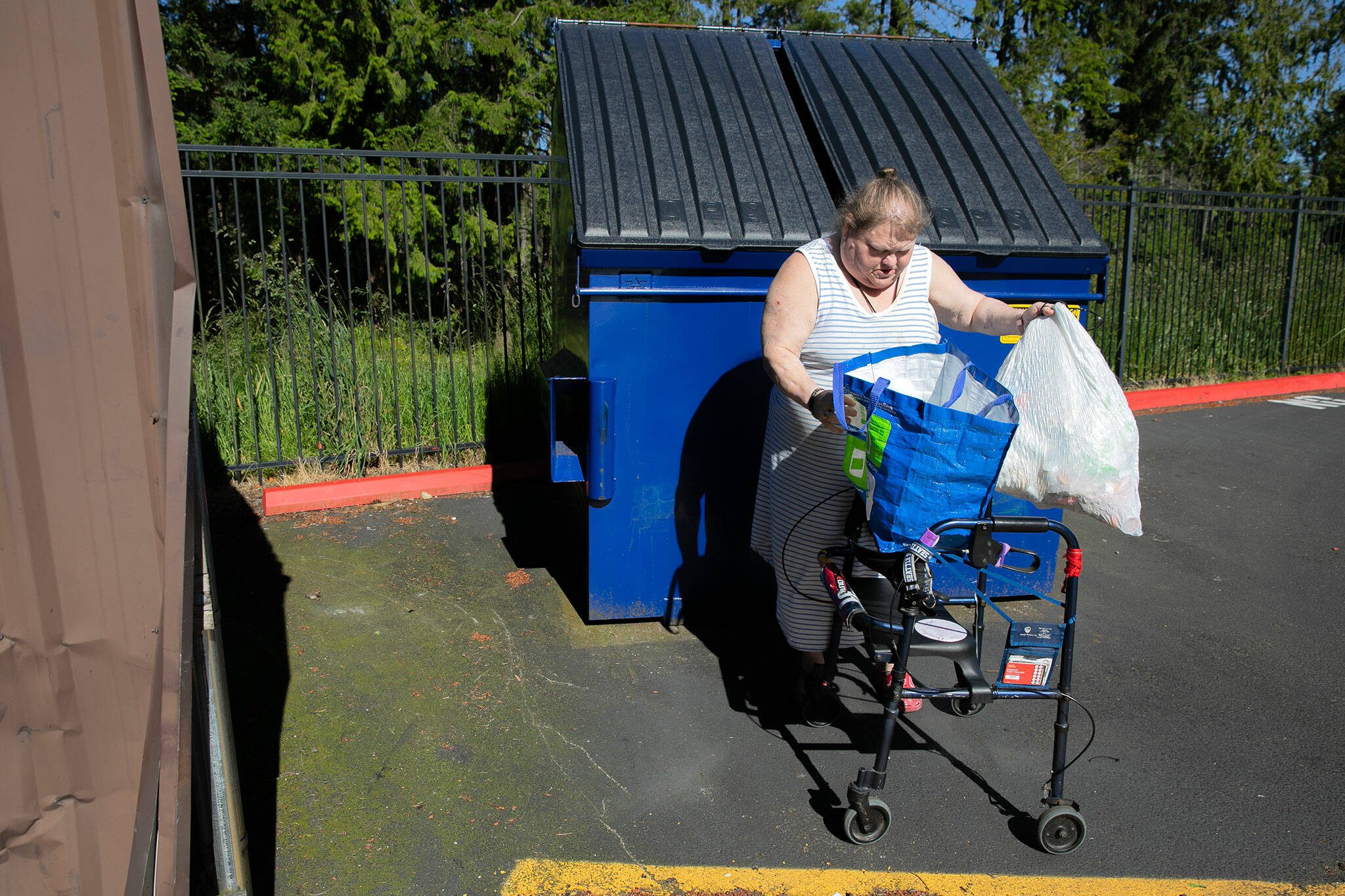 Jeanette Merkey, 54, grabs a bag of trash after emptying her recycling bag while taking out the garbage at her apartment on Friday, June 7, 2024, in Everett, Washington. Taking out the recycling can be a challenge for Merkey, who has to walk all the way across her complex to the lone recycling container that’s available. (Ryan Berry / The Herald)