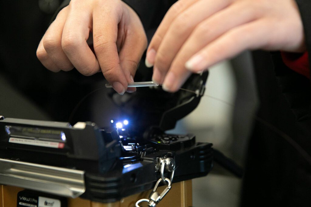 Senior Nano Portugal places a segment of heat shrink tubing into a fusion splicer during a fiber optic technician training demonstration at Sno-Isle TECH Skills Center on Tuesday, May 28, 2024, in Everett, Washington. (Ryan Berry / The Herald)

