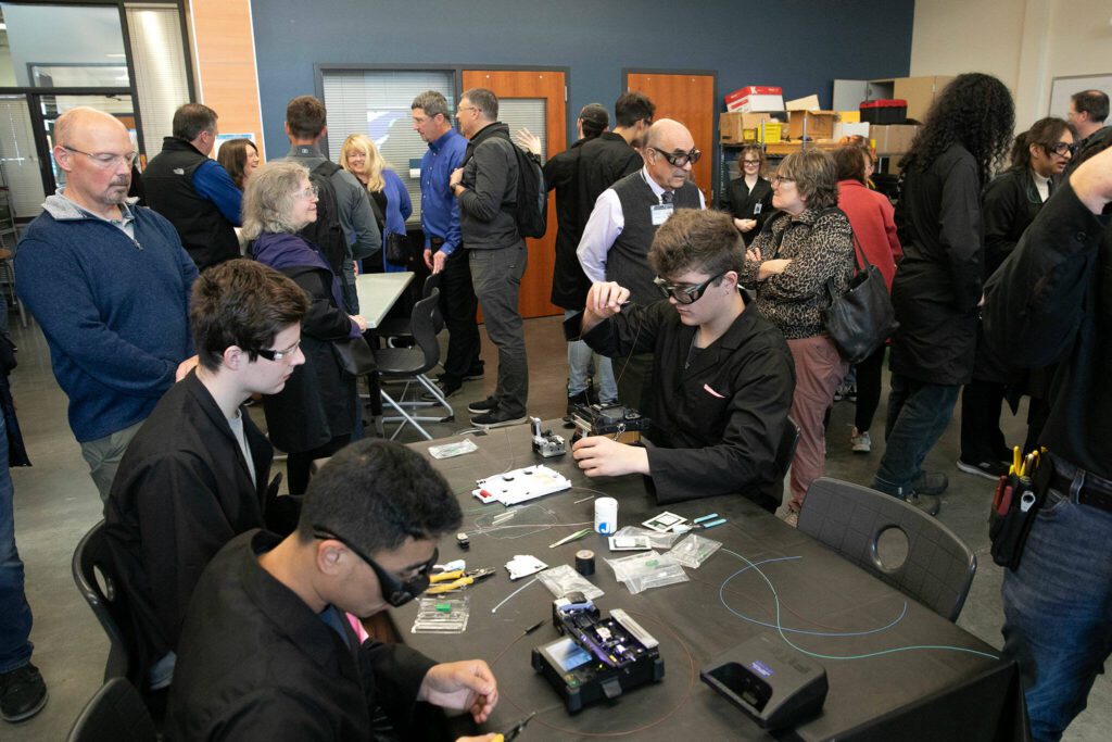 Visitors go from table to table and speak with students during a fiber optic technician training demonstration at Sno-Isle TECH Skills Center on Tuesday, May 28, 2024, in Everett, Washington. (Ryan Berry / The Herald)
