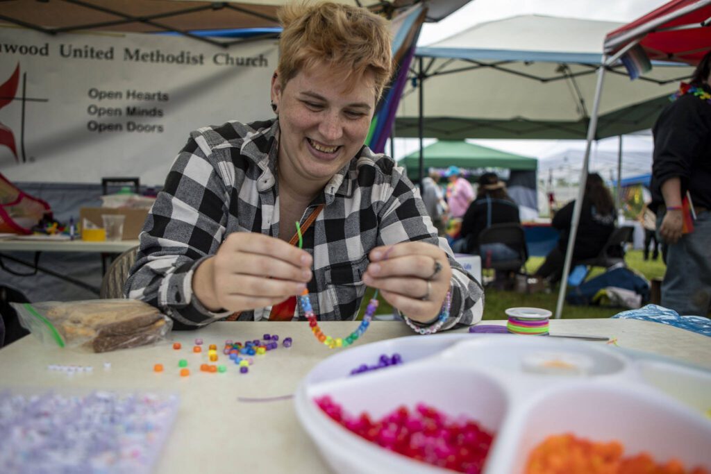 Ashton Fae makes bracelets during the Stanwood-Camano Pride event at Freedom Park in Camano, Washington on Saturday, June 1, 2024. (Annie Barker / The Herald)
