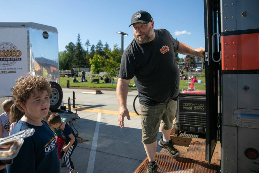 Jason Bauer, of Warpig Smokehouse, steps outside his food truck to deliver an order at the Lake Stevens Farmers Market on Wednesday, June 12, 2024, in Lake Stevens, Washington. (Ryan Berry / The Herald)
