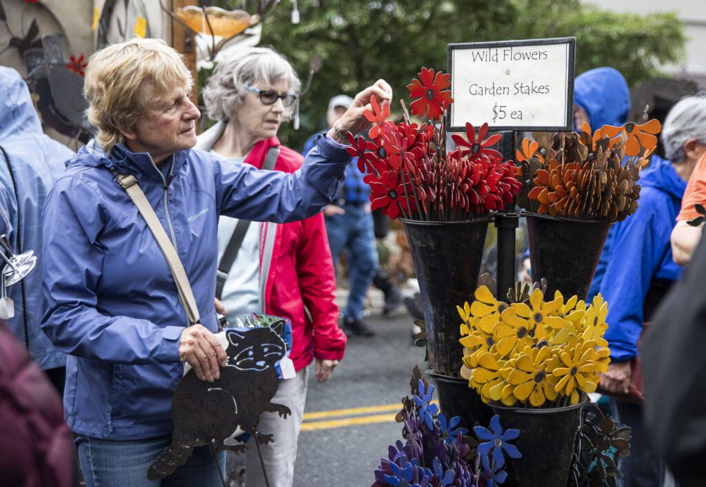 Dolly Hunnicutt holds onto a metal raccoon cutout while looking through metal wildflowers at the Freeborn Metal Art booth during the first day of Sorticulture on Friday, June 9, 2023 in Everett, Washington. (Olivia Vanni / The Herald)
