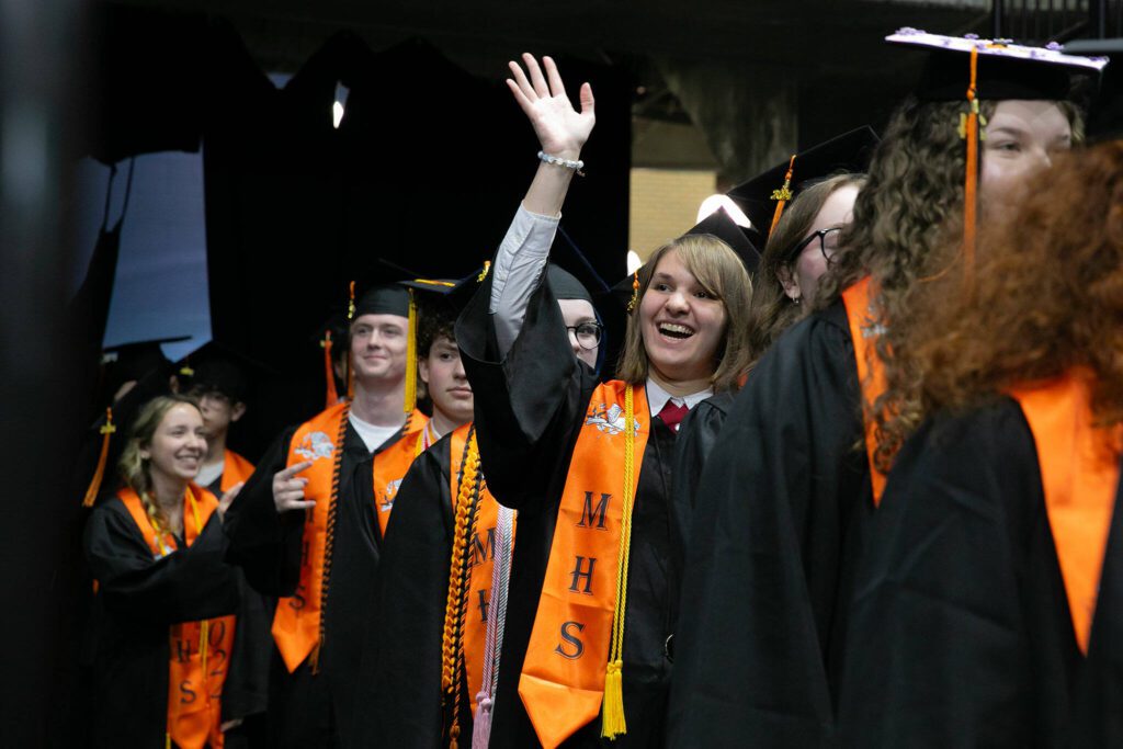 Students wait in the wings and wave to family before the processional during Monroe High School’s 2024 commencement on Wednesday, June 12, 2024, at Angel of the Winds Arena in Everett, Washington. (Ryan Berry / The Herald)

