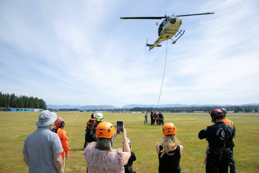 Onlookers stand by as a batch of volunteer emergency workers prepare to be lifted in an AirTEP by the Snohomish County Volunteer Search and Rescue’s Huey helicopter during an interagency training session held by Northwest Regional Aviation on Thursday, June 13, 2024, at the Arlington Airport in Arlington, Washington. (Ryan Berry / The Herald)

