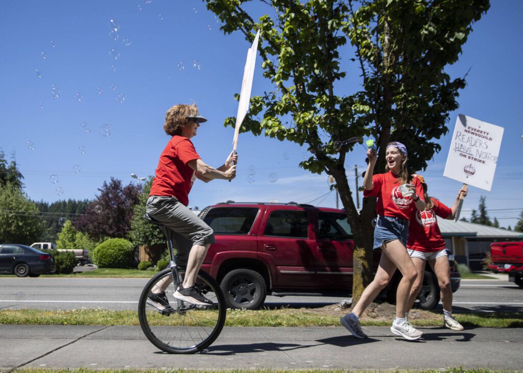 Jenelle Baumbach, right, runs ahead of Janice Podsada, left, with a bubble gun as Podsada rides her unicycle down the sidewalk along Colby Avenue during the second day of the Everett NewsGuild’s strike on Tuesday, June 25, 2024 in Everett, Washington. (Olivia Vanni / The Herald)
