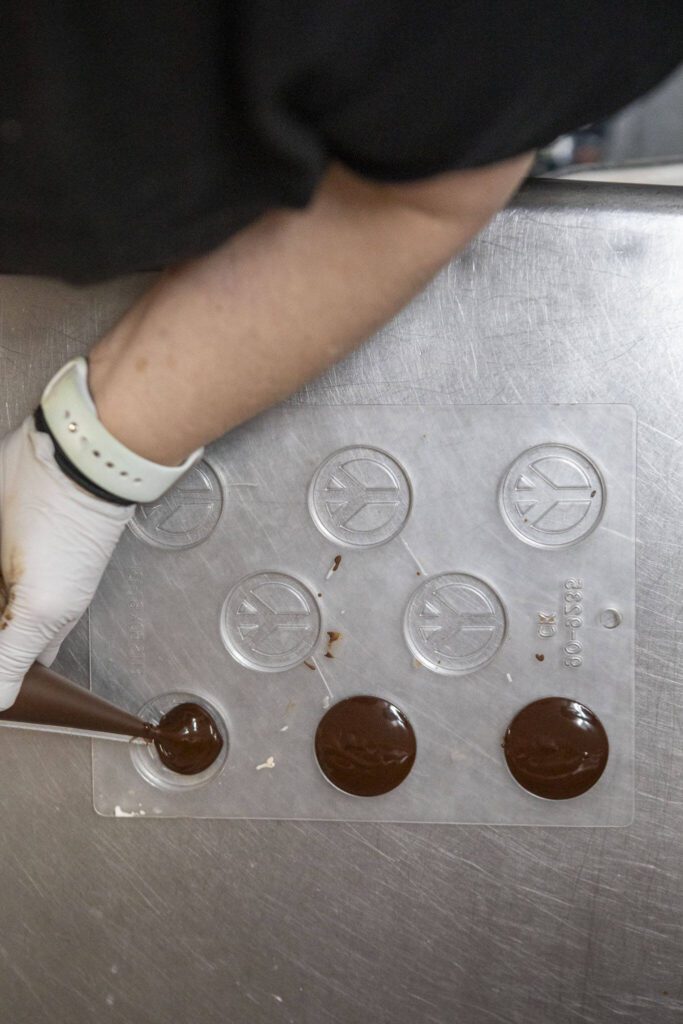 Mona Newbauer fills peace sign molds with chocolate inside her store Sweet Mona’s Chocolates on March 21, 2024 in Langley. (Annie Barker / The Herald)

