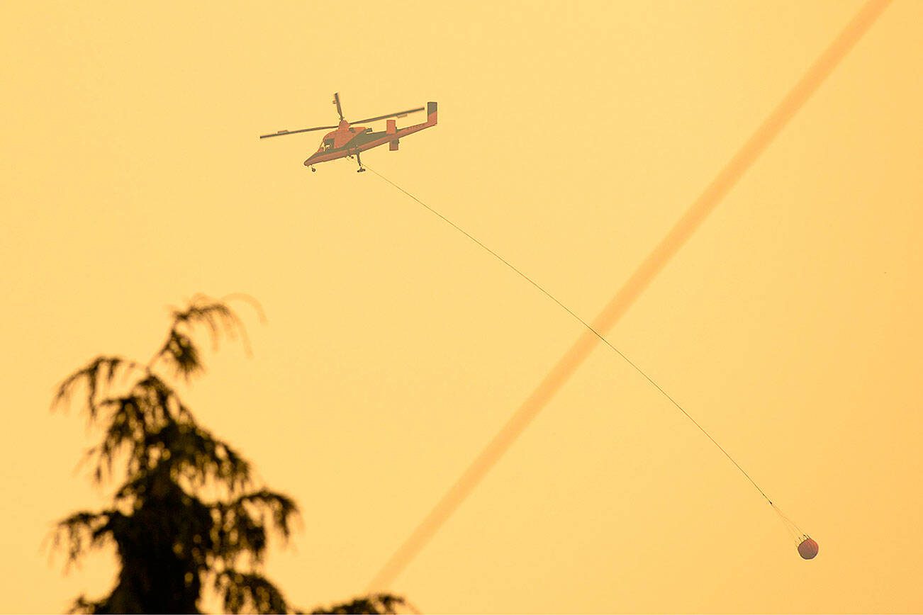 A firefighting helicopter carries a bucket of water from a nearby river to the Bolt Creek Fire on Sept. 10, 2022, on U.S. 2 near Index, Washington. (Ryan Berry / The Herald)