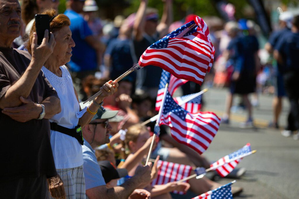 Members of the crowd wave flags during Everett’s Fourth of July Parade on Thursday, July 4, 2024, in downtown Everett, Washington. (Ryan Berry / The Herald)
