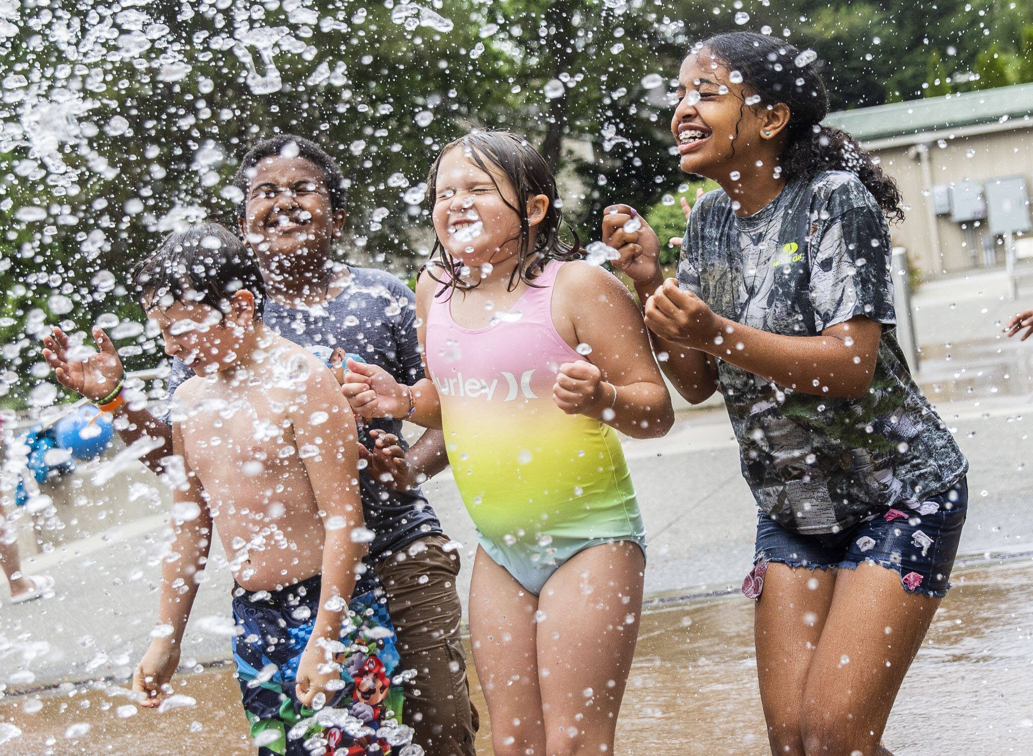 Oliver Fitting, 8, (left to right) Armon Desta, 11, and Capri Fitting, 9, and Hermela Desta, 12, close their eyes and brace for a large rush of water to be dumped on them at Hazel Miller Spray Park on Wednesday, June 26, 2024, in Edmonds, Washington. (Olivia Vanni / The Herald)