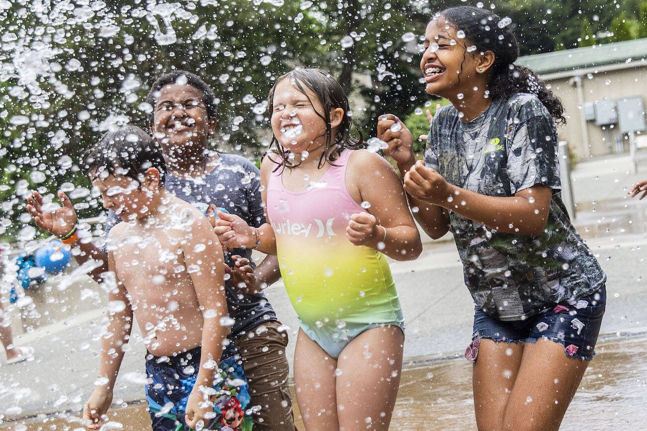 Oliver Fitting, 8, (left to right) Armon Desta, 11, and Capri Fitting, 9, and Hermela Desta, 12, close their eyes and brace for a large rush of water to be dumped on them at Hazel Miller Spray Park on Wednesday, June 26, 2024 in Edmonds, Washington. (Olivia Vanni / The Herald)