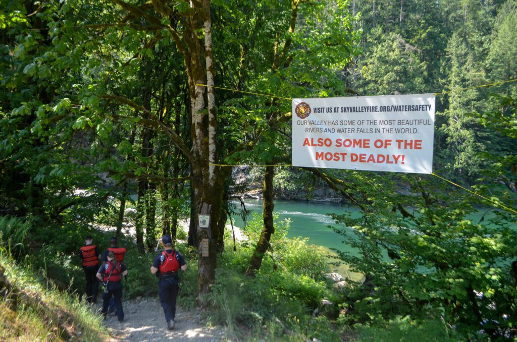 Sky Valley firefighters descend down a trail to Eagle Falls, passing a sign warning visitors about the dangerous waters below on Wednesday, July 10, 2024, near Index, Washington. (Jordan Hansen / The Herald)
