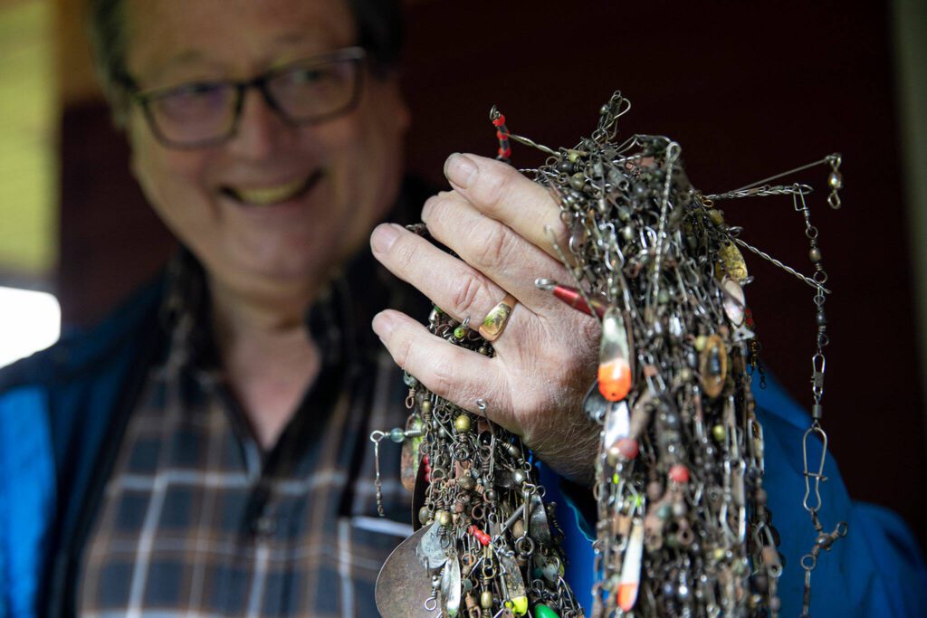 Doug Ewing proudly holds up a giant “necklace” of fishing lures he has pulled from the depths of the Snohomish River Thursday, May 19, 2022, at his home in Snohomish, Washington. Ewing said if he finds good quality lures, he tries to give them away to people who appear to be fishing responsibly. (Ryan Berry / The Herald)
