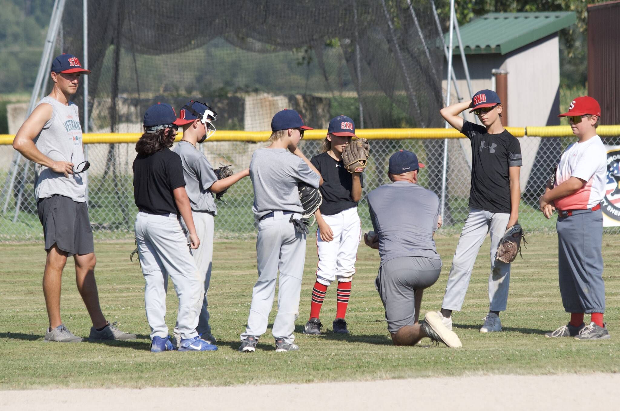 Boys Snohomish Little League 8-10 coach Aaron Barstad (kneeling) talks to the outfield during practice at the Snohomish Little League Complex in Snohomish, Washington on Thursday, July 18, 2024. Barstad’s team claimed the Washington District 1 Little League title, securing a spot in the 2024 Washington State 8-10 Baseball tournament held July 20-27 at the North Kitsap League Complex in Poulsbo, Washington. (Taras McCurdie / The Herald)