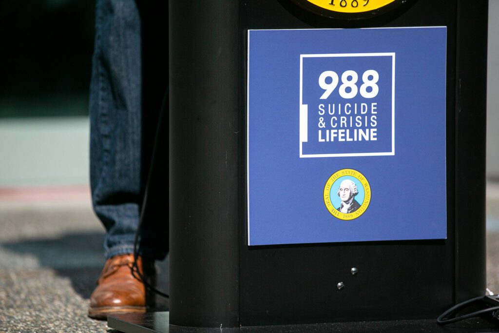 A 988 Suicide & Crisis Lifeline poster hangs from a lectern as Gov. Jay Inslee addresses a crowd about mental health services in Washington on Thursday, July 28, 2022, in Everett, Washington. (Ryan Berry / The Herald)
