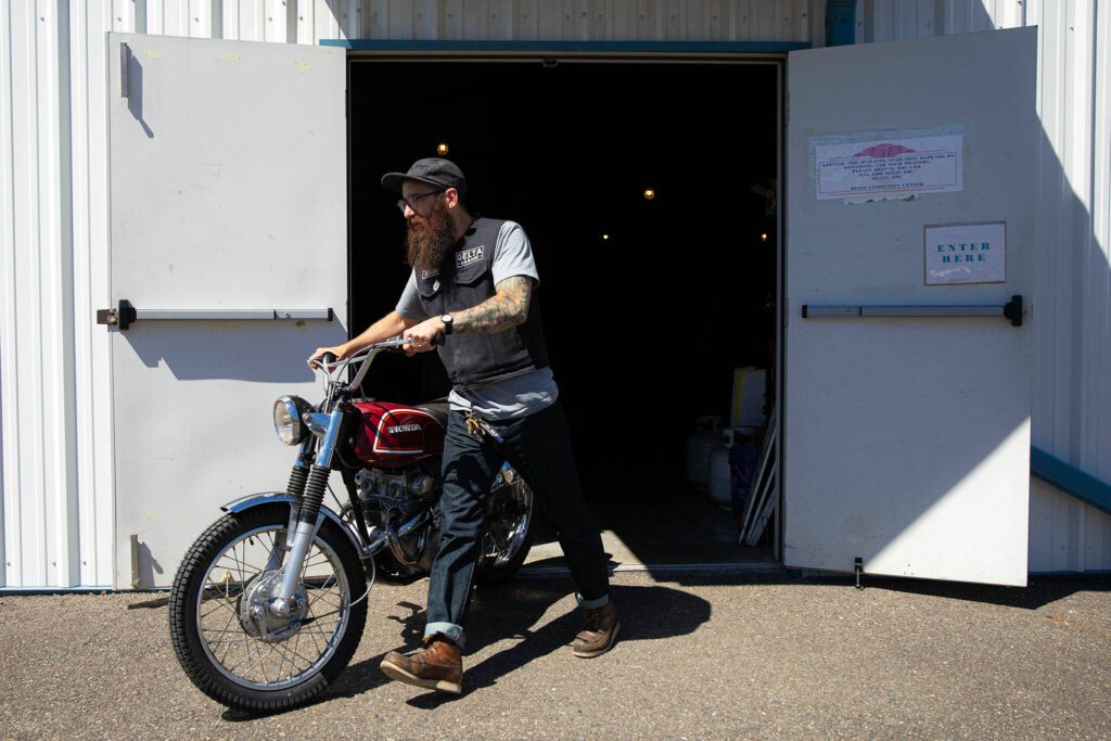 Crew Chief Jared Kalinski walks a Honda CL175 project bike over to the work area at Delta Garage on July 5 in Everett. The program has received around ten bikes as donations in just a year’s time. (Ryan Berry / The Herald)
